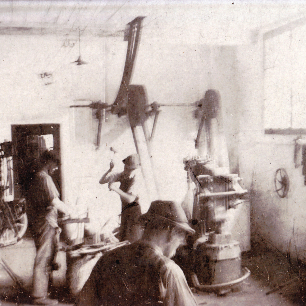 Fotografie um 1945. Einblick in die Schmiede. Im rechten Bildhintergrund befindet sich der Federhammer. Darüber die Transmissionen vom Wasserrad. Blick von der Schmiede durch die niedere Türe in die Werkstatt.